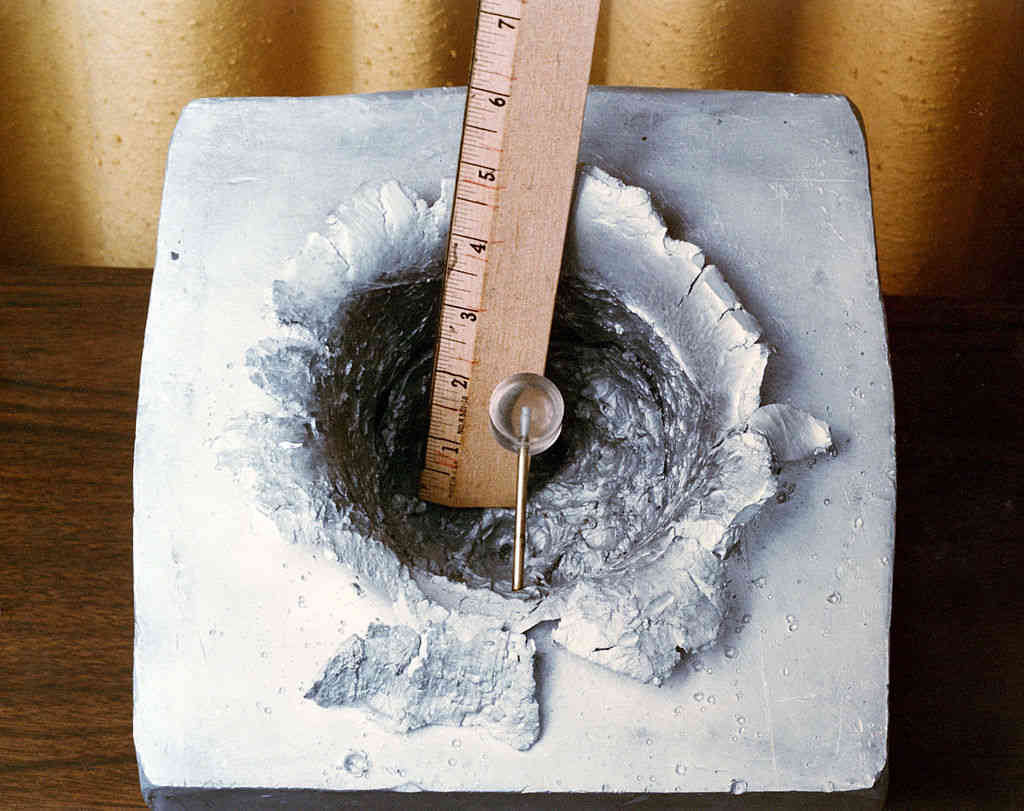 A large impact crater in an aluminium block caused by a 7 gram plastic pellet fired at 7km/s.